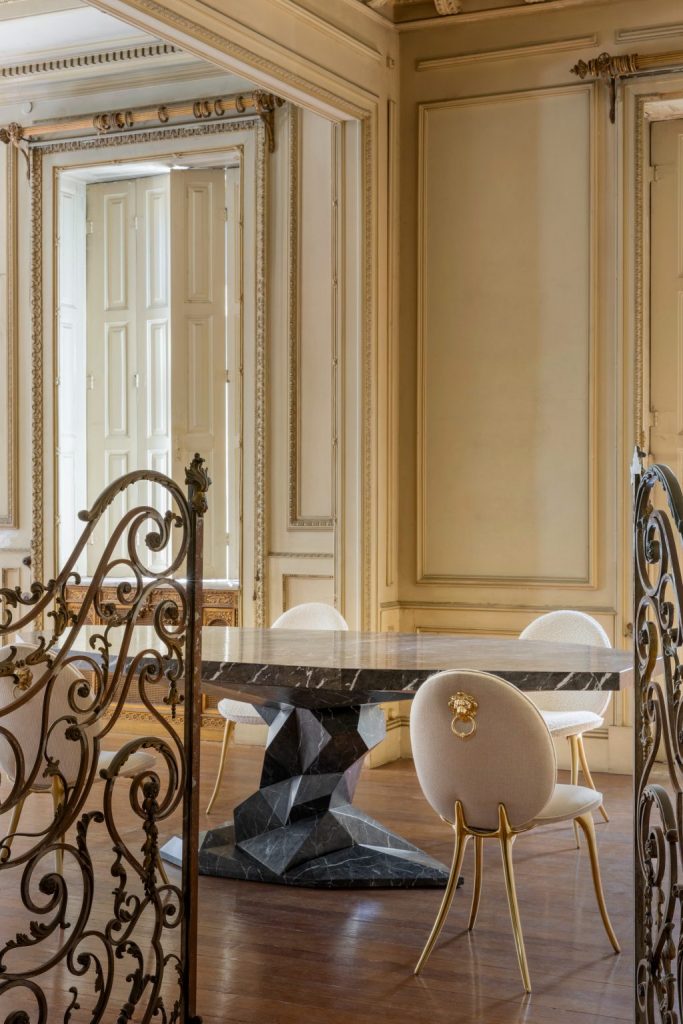 intimate luxury- contemporany dining room with yellow walls and large door, marble dining table and white chairs with gold details